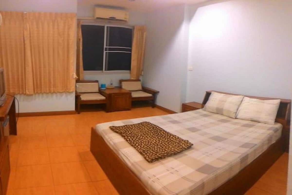 Un dormitorio con cama, una silla, una mesita y una ventana con cortinas.