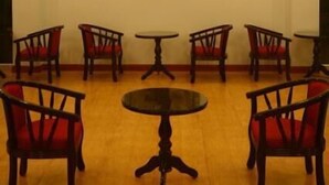 Ein Zimmer mit sechs Holzsesseln und einem runden Tisch, einem gerahmten Porträt an der Wand und Einbauleuchten.