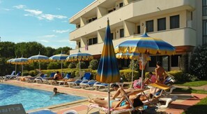 A pool area with lounge chairs and umbrellas, a building with balconies, and a clear sky. - Eurobeach Residence (Cavallino-Treporti)