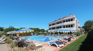 A pool area with lounge chairs and umbrellas, a large building in the background, and a clear blue sky. - Eurobeach Residence (Cavallino-Treporti)