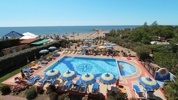 Un área de piscina con sillones de descanso y sombrillas, rodeada de vegetación y vistas al mar.