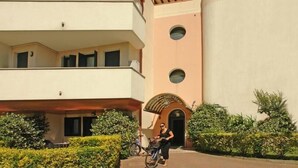 Un edificio de varios pisos con un balcón, una bicicleta estacionada frente a él y setos bien cuidados.