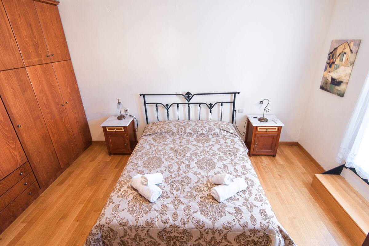 Un dormitorio con cama, armario de madera, dos mesitas de noche y un cuadro en la pared.