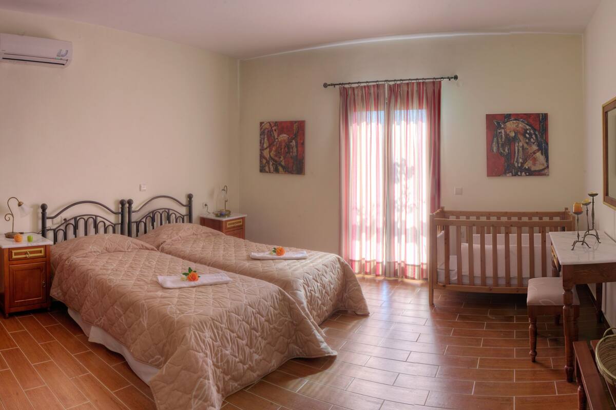 Un dormitorio con dos camas, una cuna de madera, un escritorio con silla y obras de arte en las paredes.