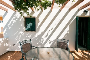 Eine Außenpatio mit einem runden Tisch und zwei Korbstühlen, umgeben von weißen Wänden und Holzbalken.