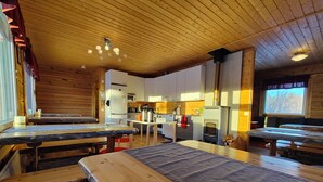 A rustic wooden interior with wooden tables and benches, a kitchen area, and a fireplace.