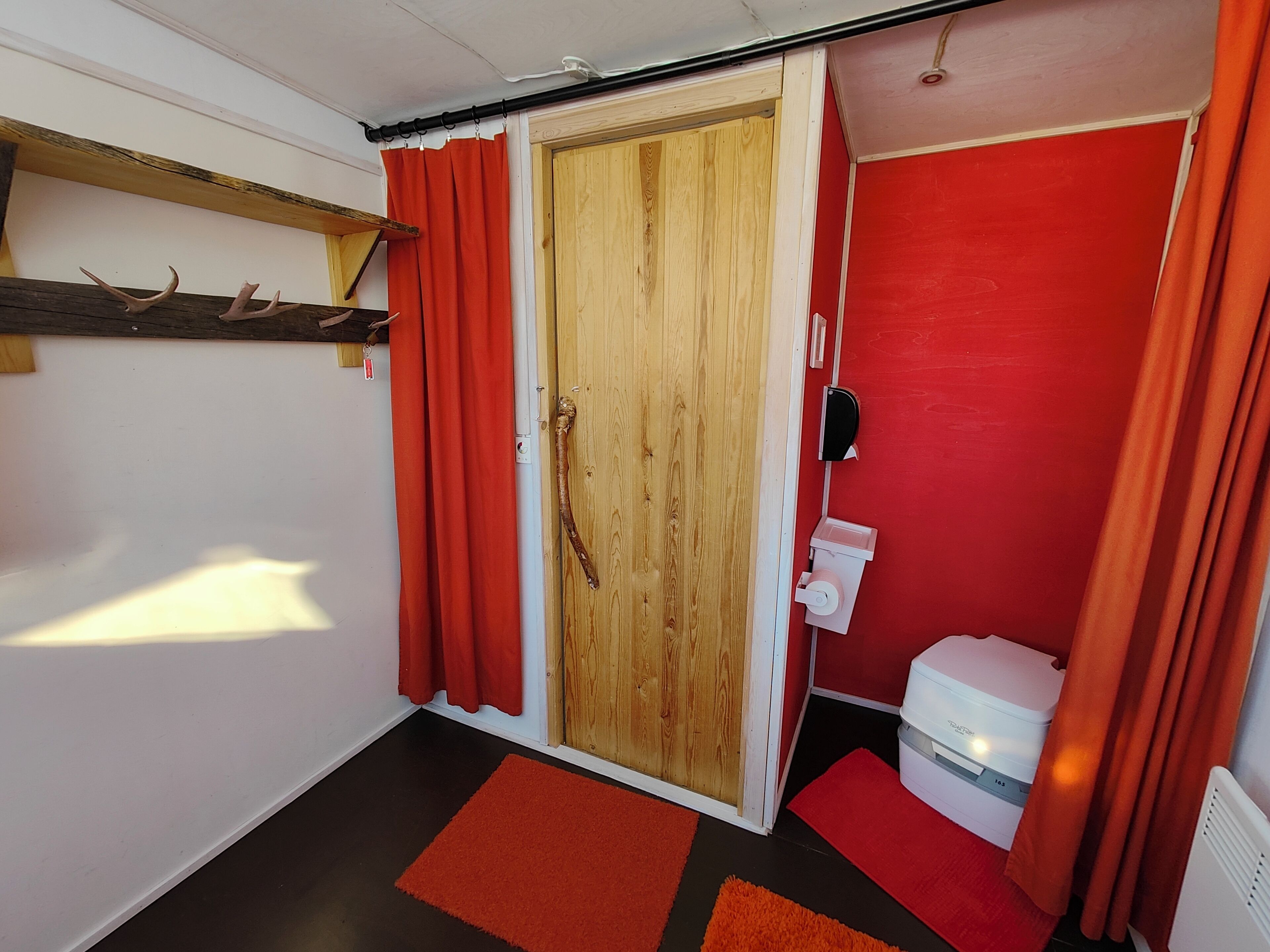 Un baño pequeño y funcional con puerta de madera, paredes rojas y un inodoro blanco.