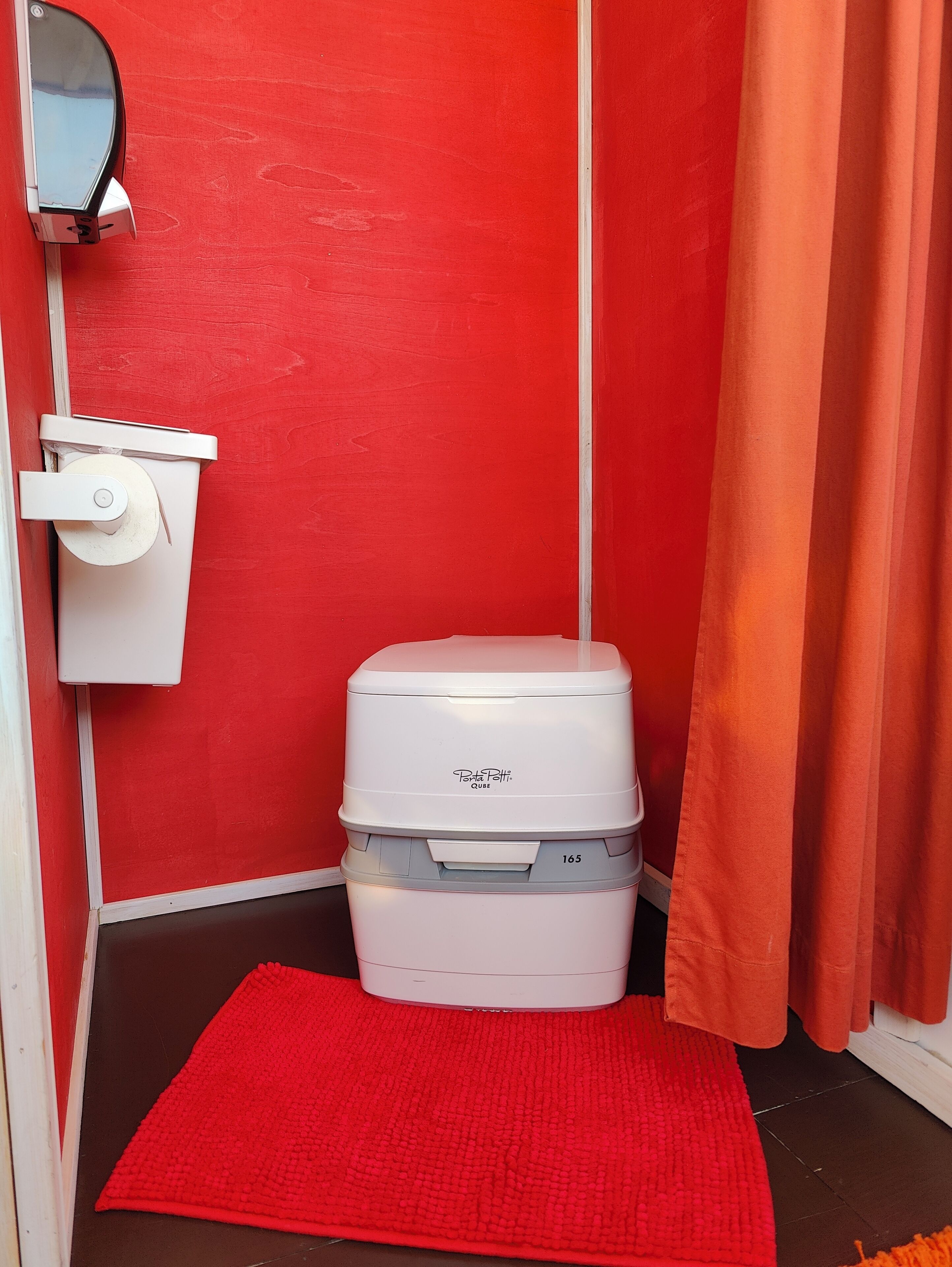 Une petite salle de bain avec un mur rouge, des toilettes blanches et un tapis rouge sur le sol.