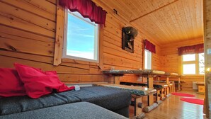 A cozy cabin with wooden walls and floors, a sofa with red cushions, and a dining area with benches.