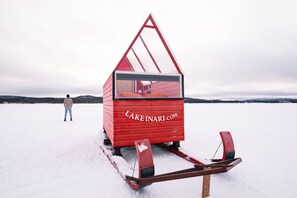 A red wooden sled house with a person standing in the background.