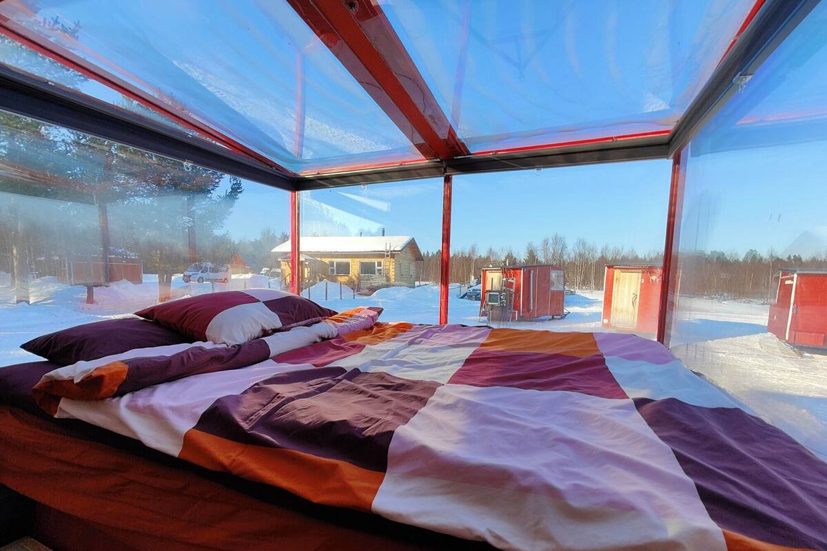Una cama con colcha en una habitación con ventanales amplios.
