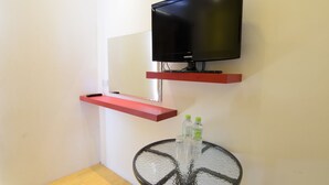 Una habitación moderna con un televisor montado en un estante rojo, una pequeña mesa redonda con dos botellas y un estante rojo debajo del televisor.
