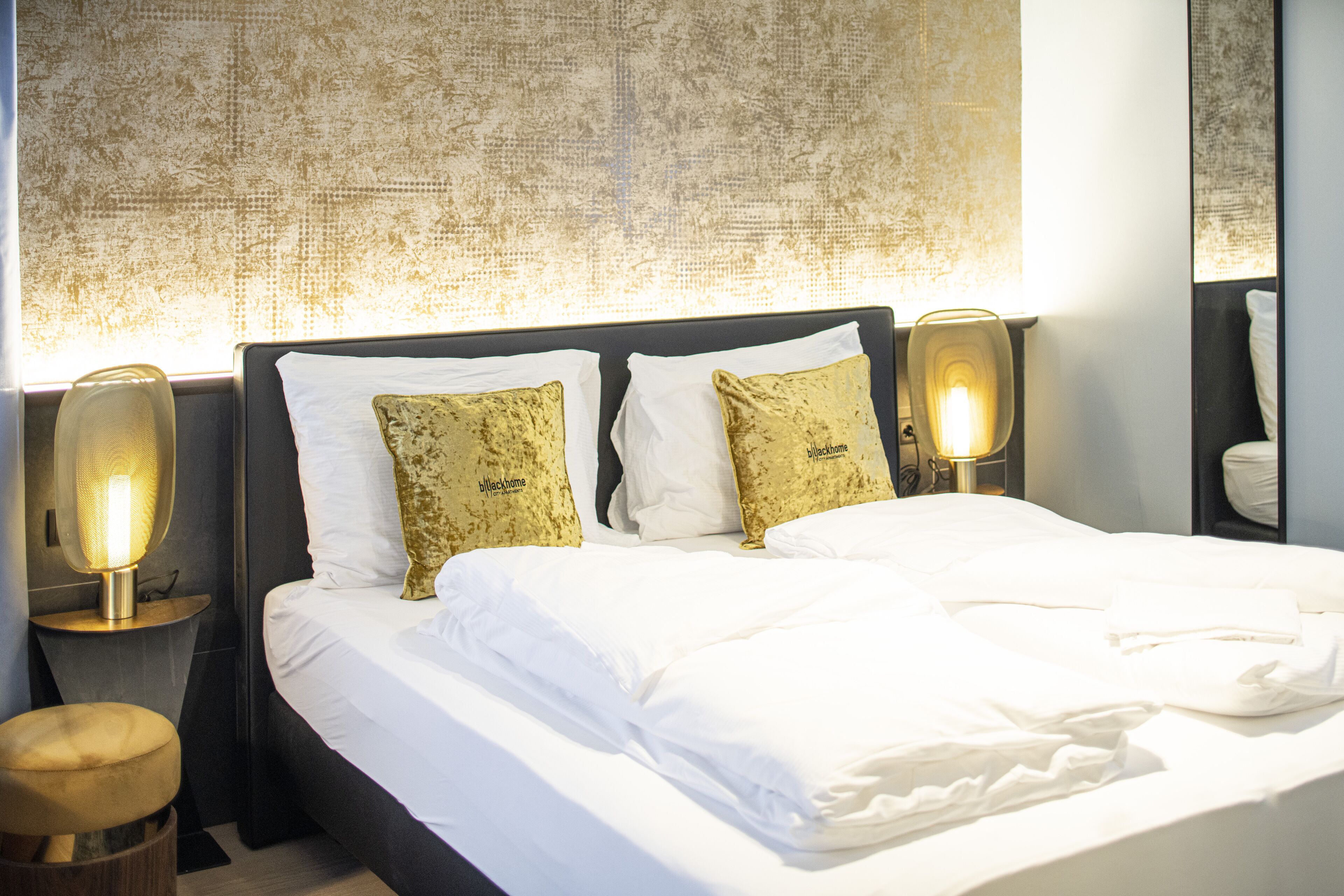 A neatly made bed with white linens and two decorative pillows, flanked by two bedside lamps on wooden nightstands.
