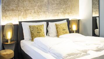 A neatly made bed with white linens and two decorative pillows, flanked by two bedside lamps on wooden nightstands.