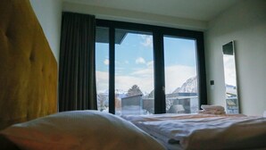 A hotel room with a bed, a window with a view of mountains, and a mirror on the wall.