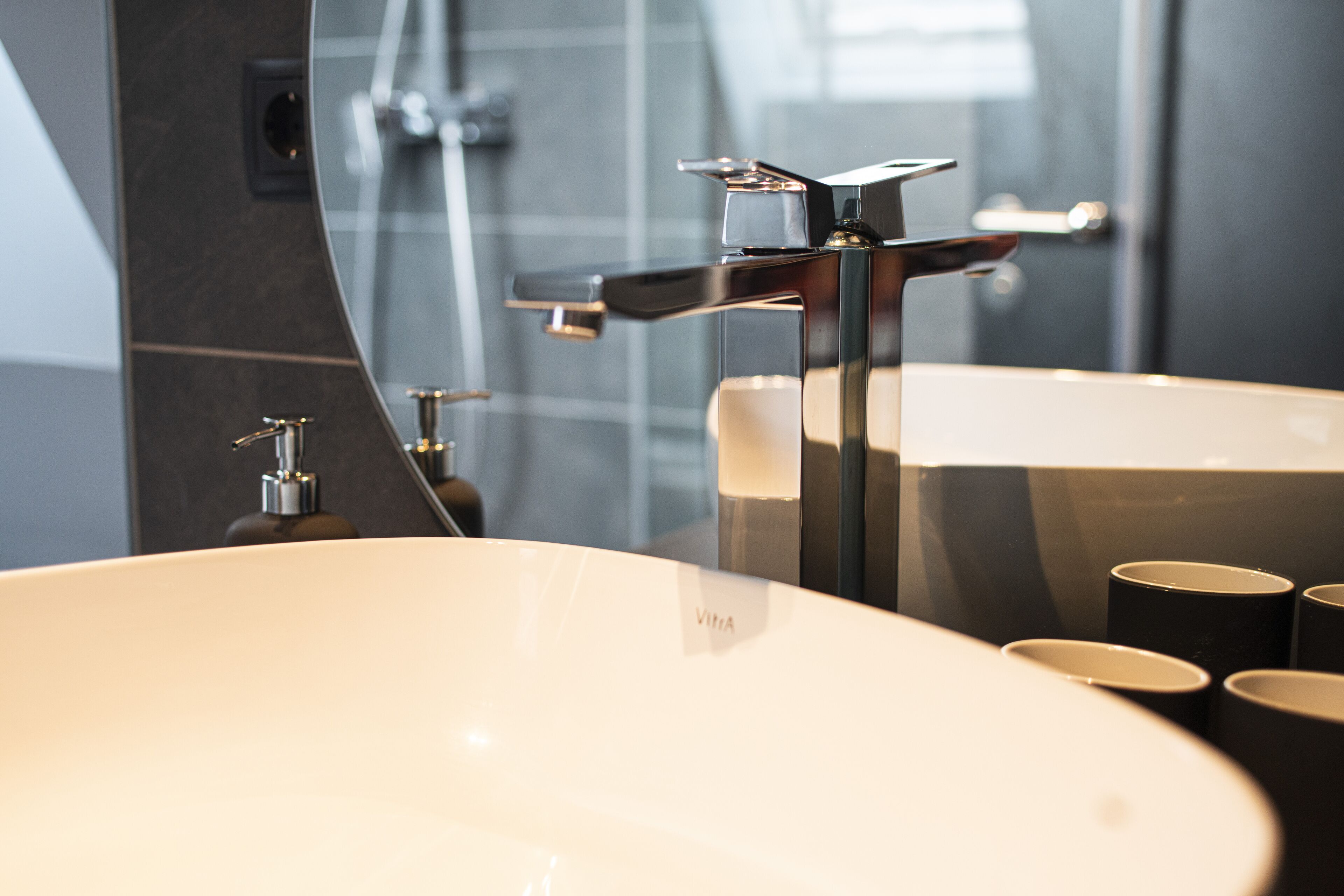 Ein modernes Badezimmer mit einem großen, ovalen Waschbecken, einem Chromarmaturen und einem Spiegel, der den Raum widerspiegelt.