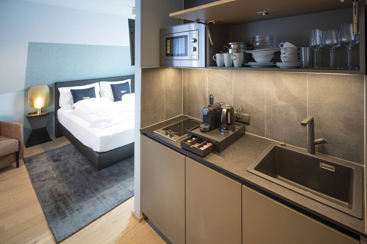 Ein modernes Hotelzimmer mit Küchenzeile, einem Bett und einer kleinen Sitzecke.