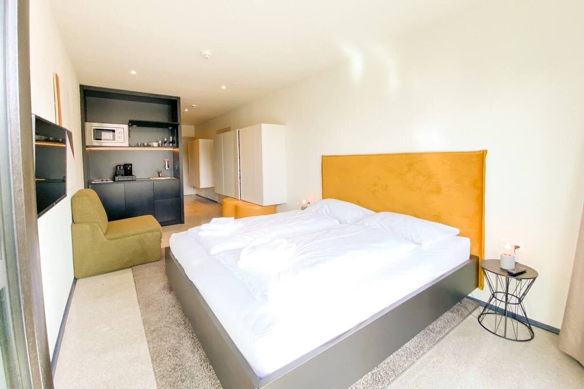 Ein modernes Hotelzimmer mit einem großen Bett, einer kleinen Küchenzeile, einer Sitzecke und einem separaten Badezimmer.
