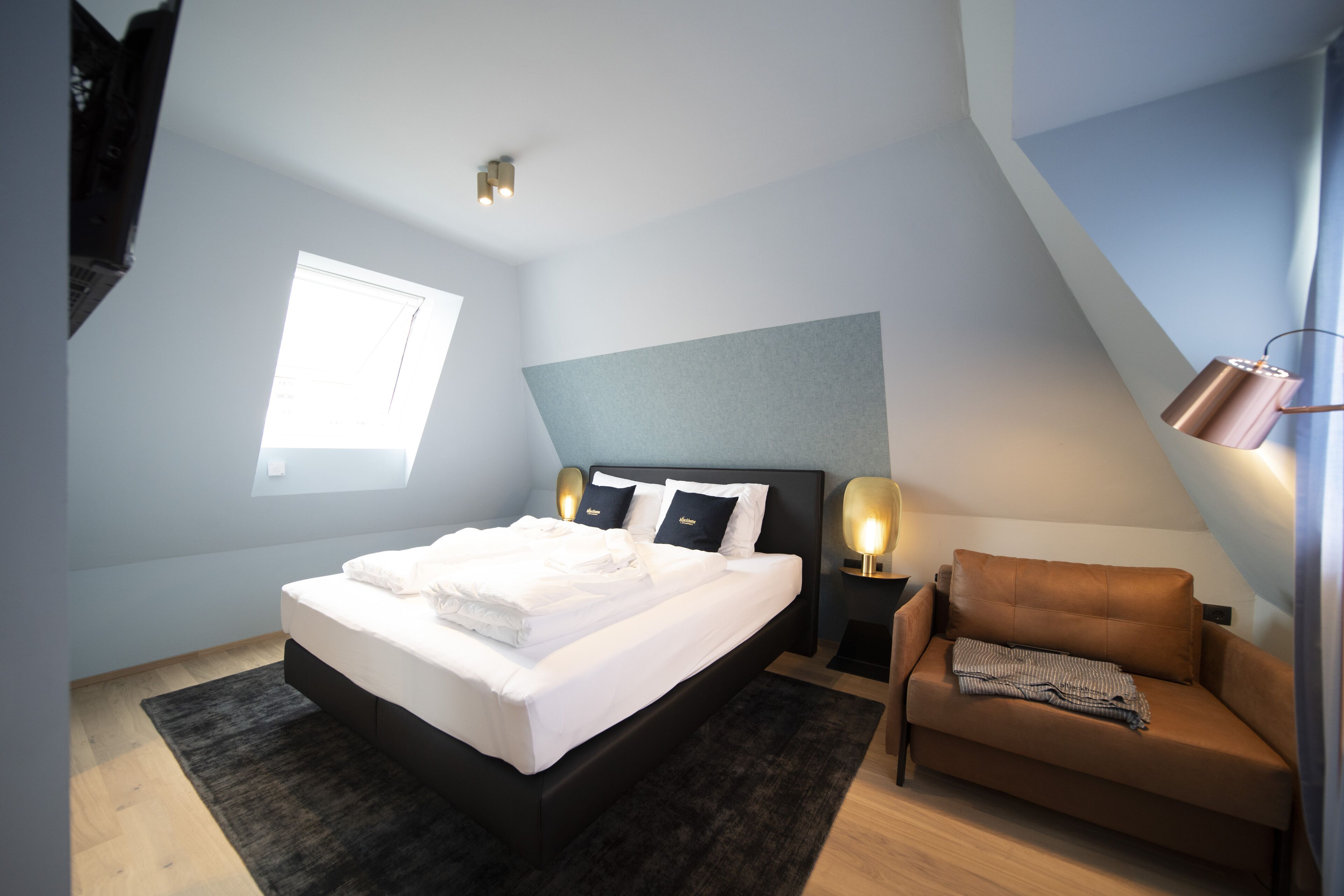 Un dormitorio con cama, sofá, ventana y lámpara.