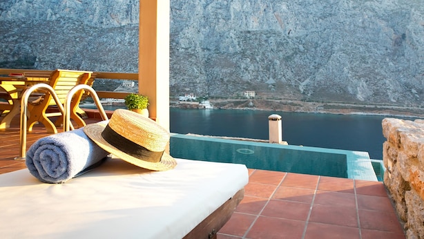 Une terrasse ensoleillée avec une piscine, un fauteuil de relaxation, une serviette enroulée et un chapeau de paille.