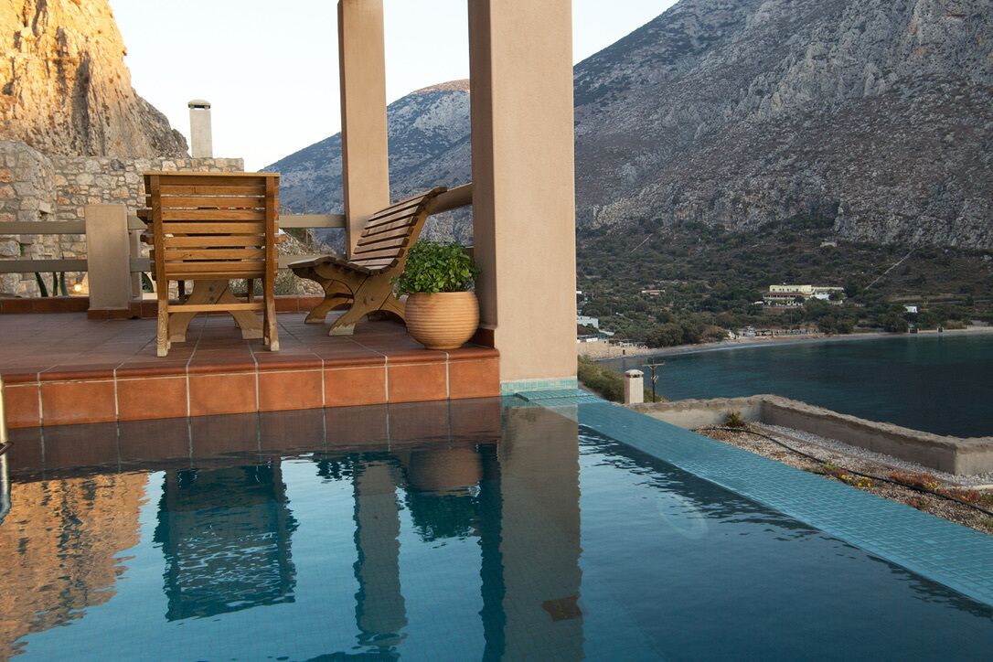 Una piscina infinita con una silla de madera y una planta en maceta, con vistas a un paisaje montañoso.