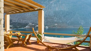 Une terrasse avec une table et des chaises en bois, un hamac et une vue sur un lac et des montagnes.