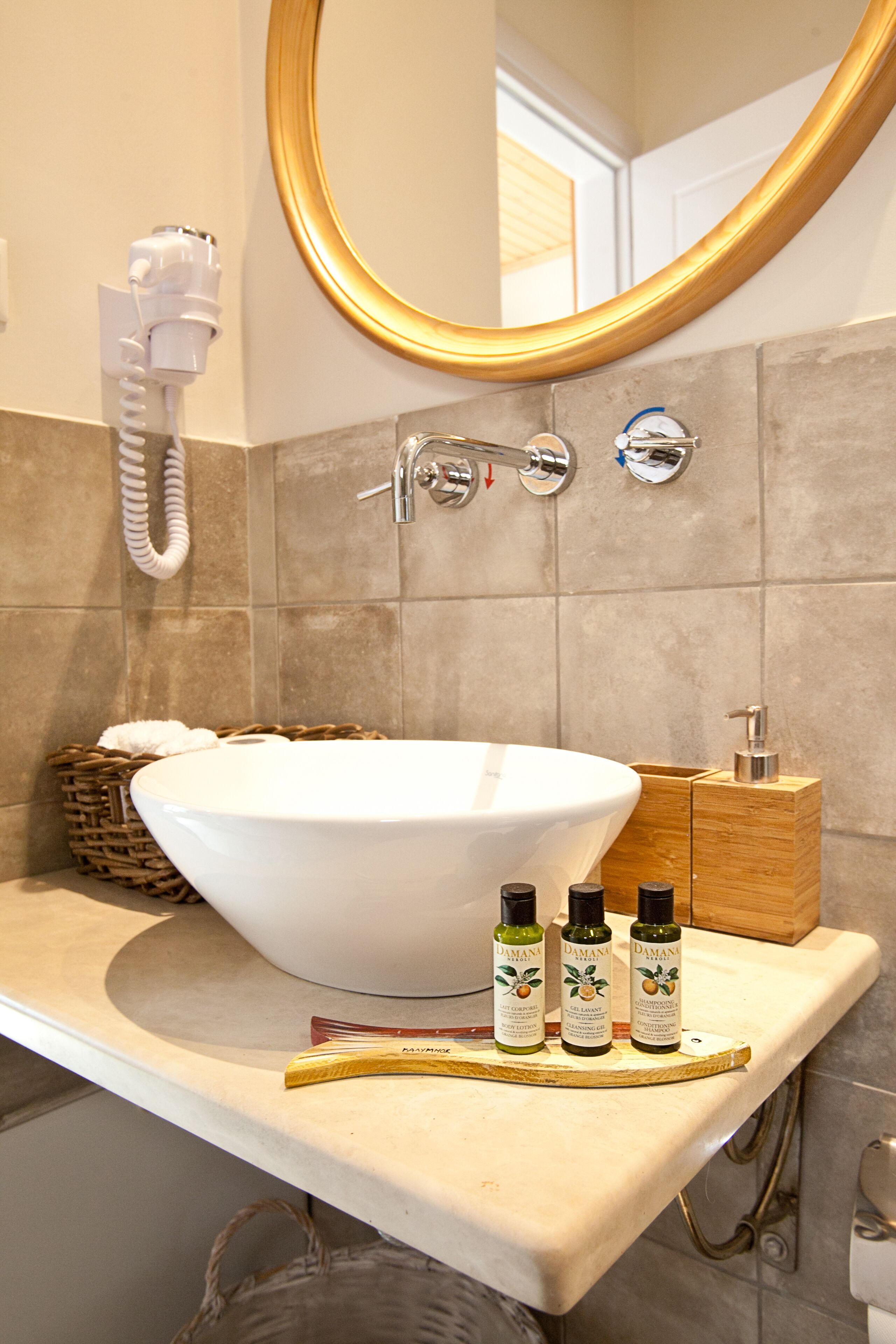 A bathroom with a large white sink, a gold-framed mirror, and a wooden cabinet with toiletries.