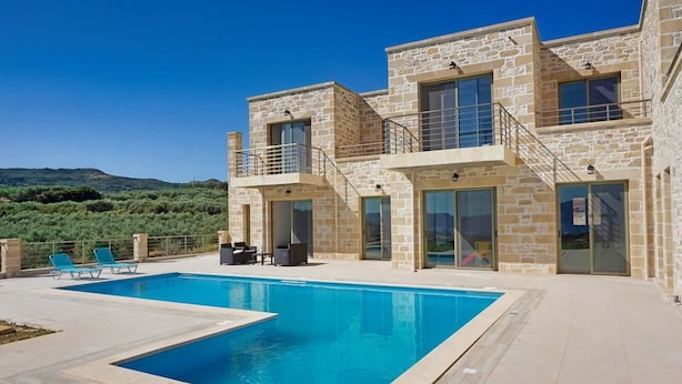 Une maison en pierre à deux étages, dotée d’une piscine, d’un espace extérieur aménagé et offrant une vue sur les collines.