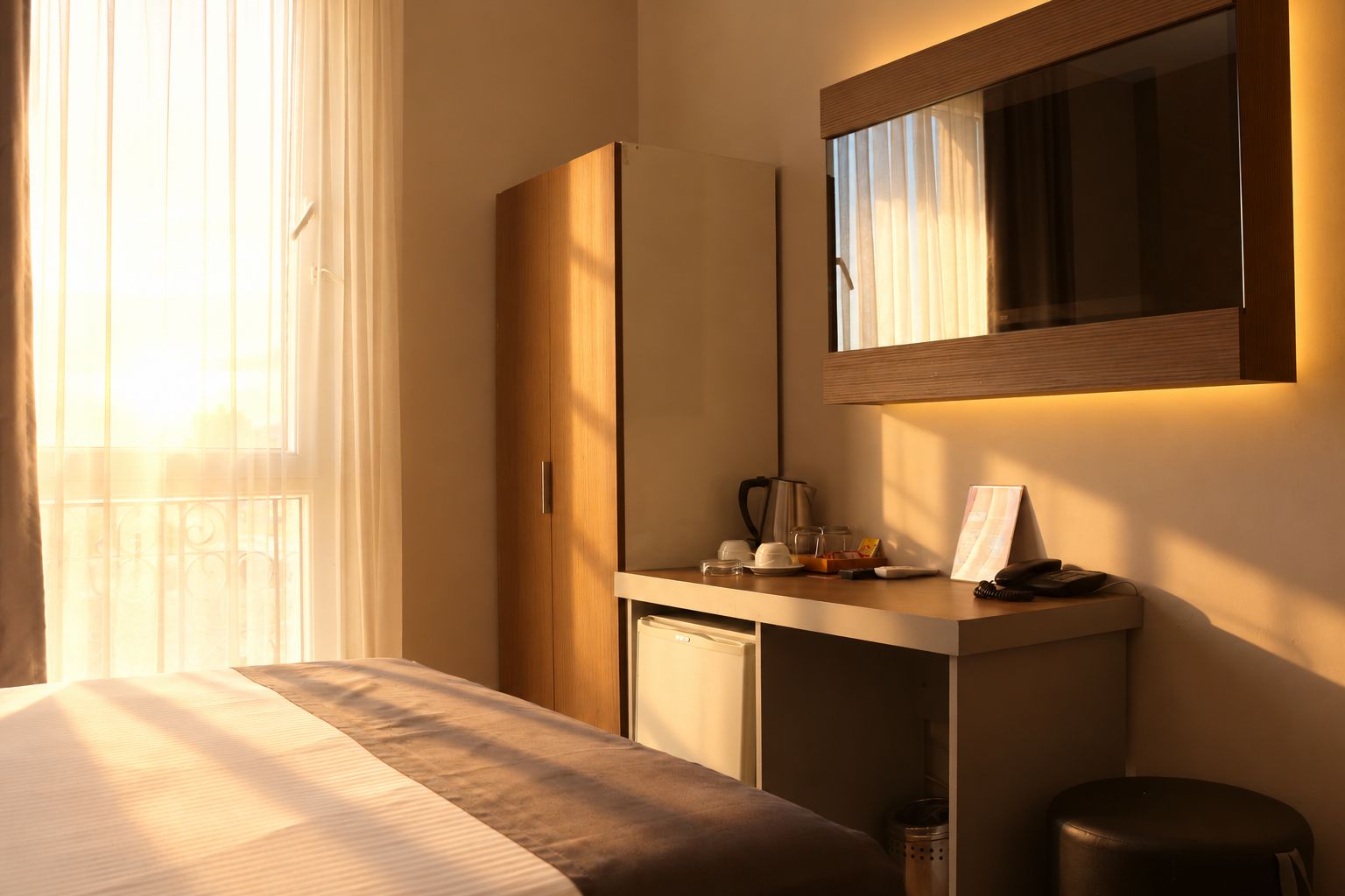 Una habitación de hotel con una cama, un escritorio con espejo, un archivador pequeño y un cubo de basura.
