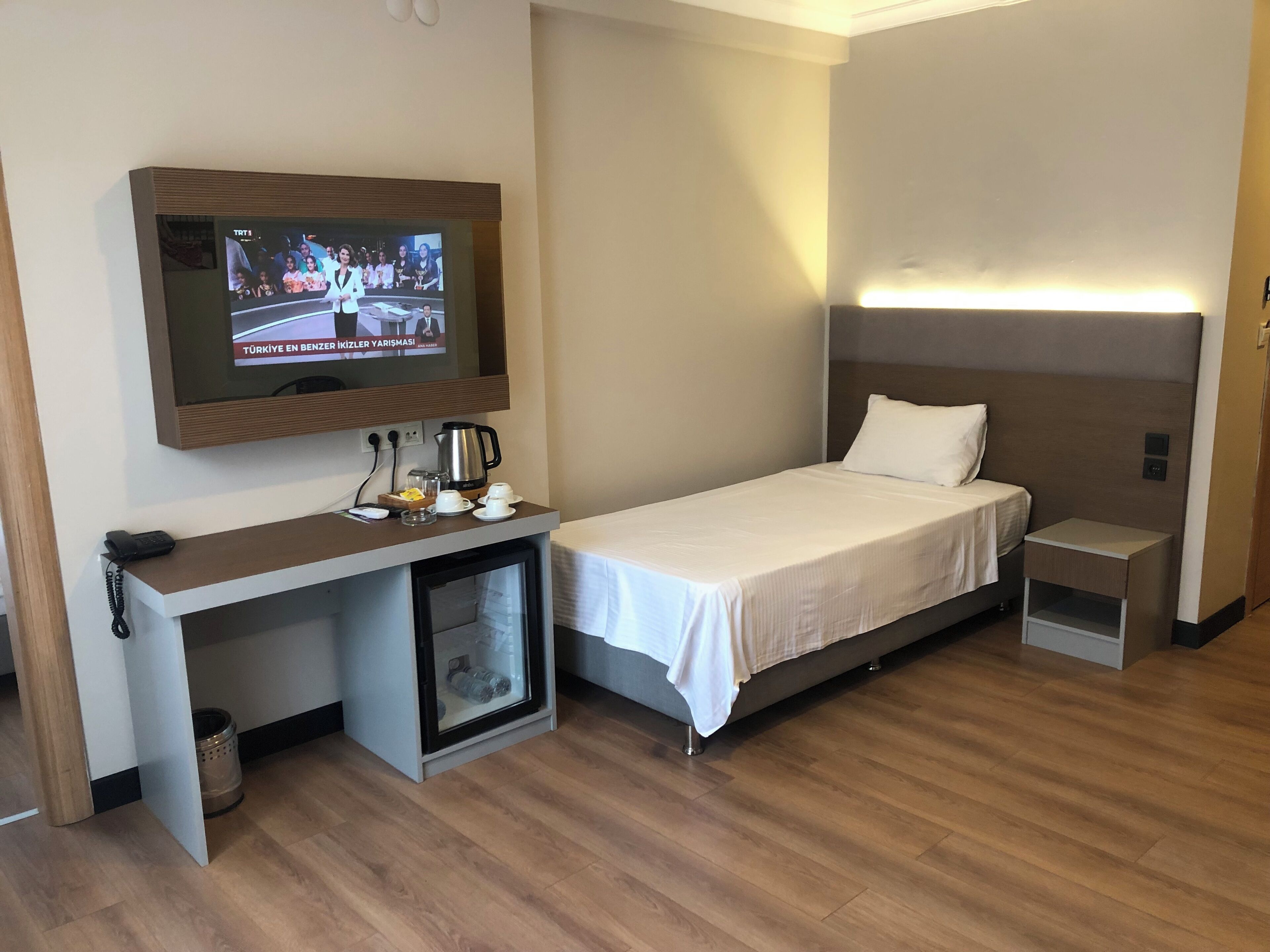 A hotel room with a bed, a desk with a television, a coffee maker, and a small cabinet.