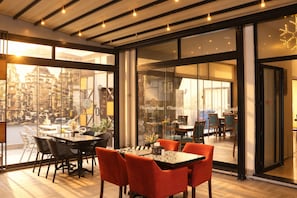 A modern hotel interior with a dining area featuring a table and chairs, large windows with a view of the city, and a glass partition with the hotel name. - Niconya Port Suite&Hotel (Istanbul)