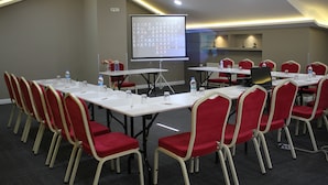 Une salle de conférence avec des tables blanches, des chaises rouges, un écran de projection et un distributeur d’eau.