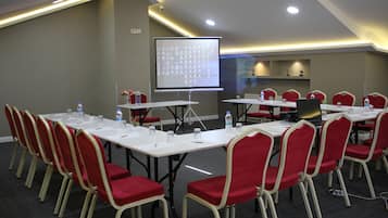 Una sala conferenze con tavoli bianchi, sedie rosse, uno schermo di proiezione e un distributore d'acqua.