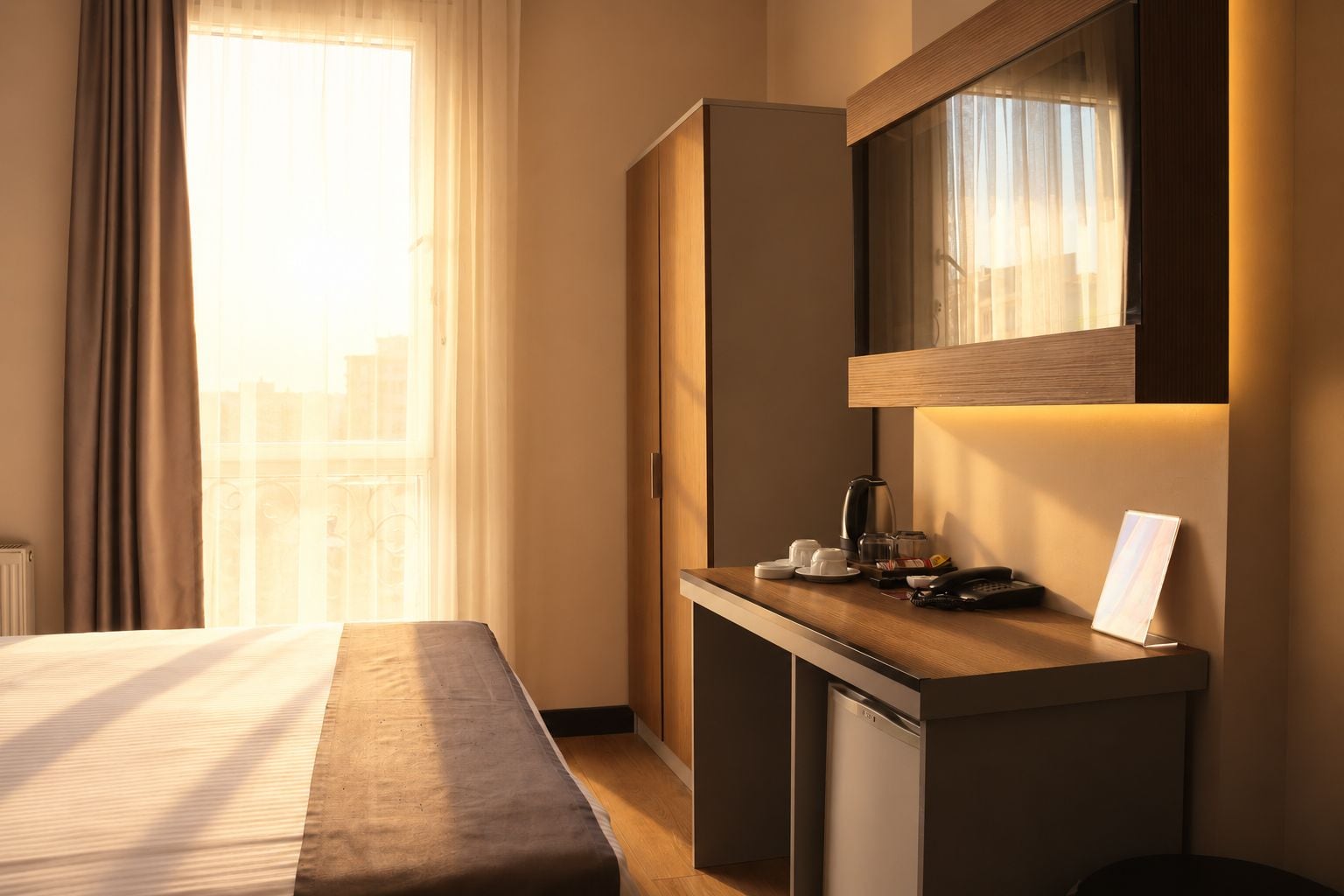 Quarto de hotel com cama, escrivaninha com telefone, cafeteira e pequeno armário.