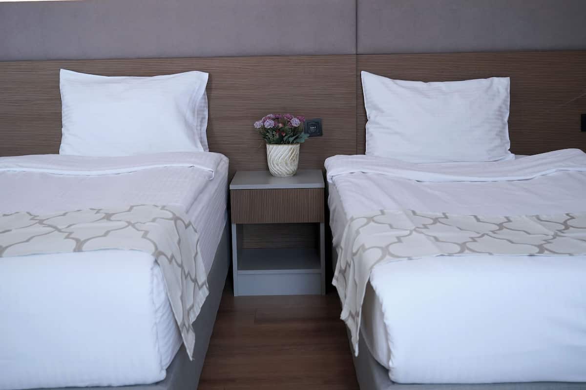 A hotel room with two beds, a nightstand with a vase of flowers, and a wooden headboard.