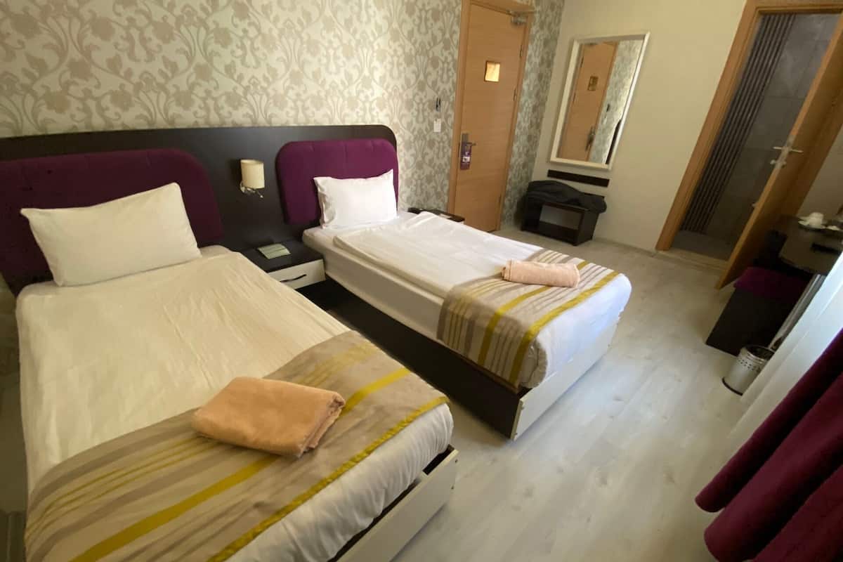 A hotel room with two beds, a nightstand, a mirror, and a door.