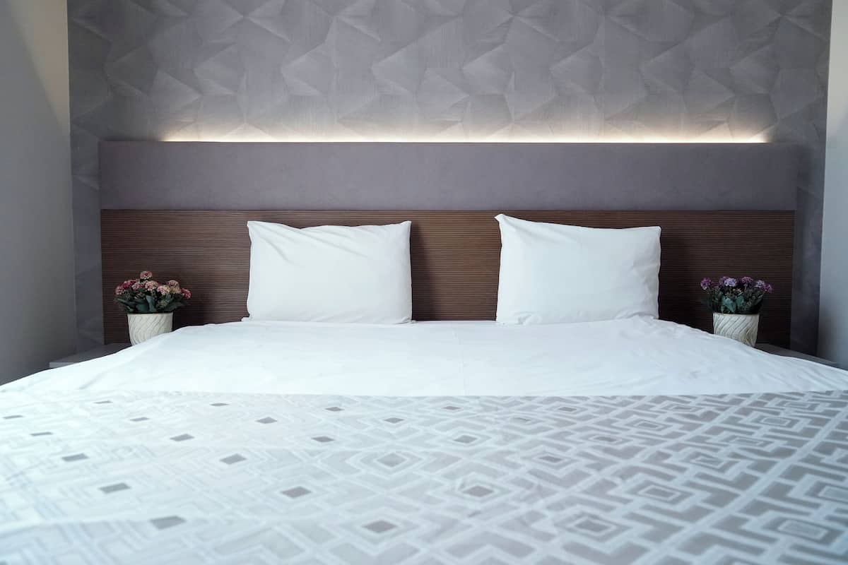 A neatly made bed with a patterned bedspread, a wooden headboard, and two bedside tables with flower vases.