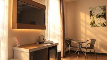 Una camera d'albergo con una scrivania, televisore, macchina del caffè e zona pranzo con sedie.
