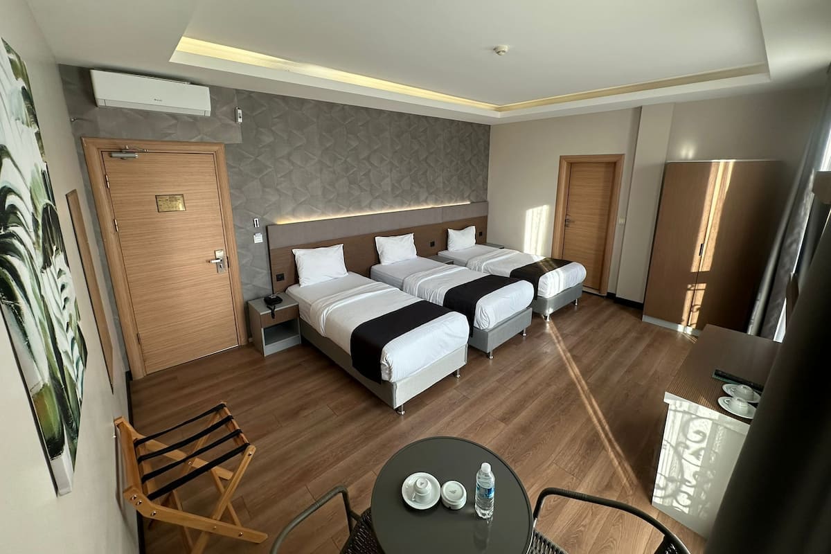 A hotel room with two beds, a desk, a chair, a table with a bottle, and a mirror.