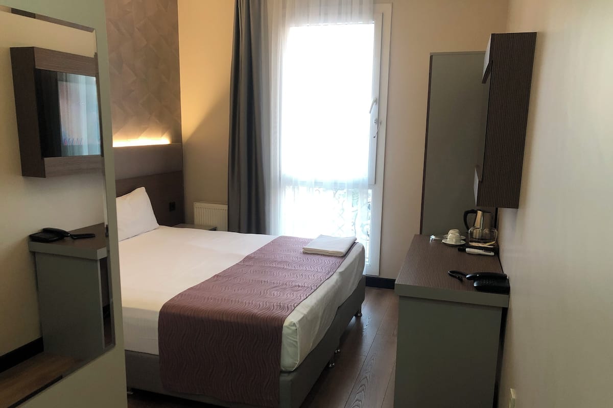 A hotel room with a bed, bedside table, and a desk with a chair.