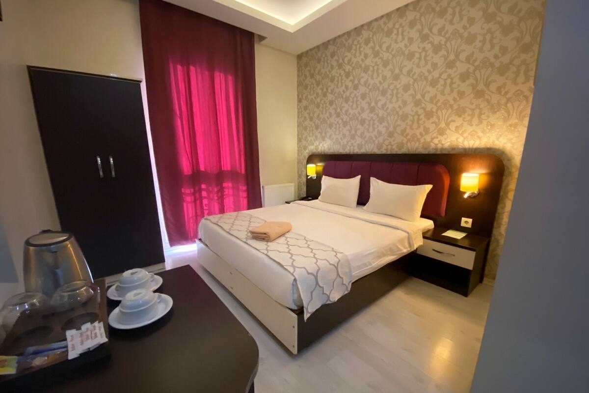 A hotel room with a bed, bedside tables, a desk with a coffee maker, and a wardrobe.