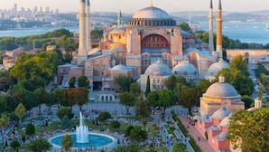 Un ensemble de bâtiments historiques comprenant plusieurs dômes et minarets, entouré d’un parc agrémenté d’une fontaine.