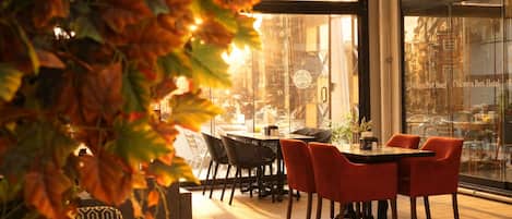 Un espace de restauration intérieur avec des tables et des chaises, un mur de verre offrant une vue sur la ville et une plante décorative au premier plan.