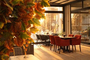 An indoor dining area with tables and chairs, a glass wall with a view of the city, and a decorative plant in the foreground. - Niconya Port Suite&Hotel (Istanbul)