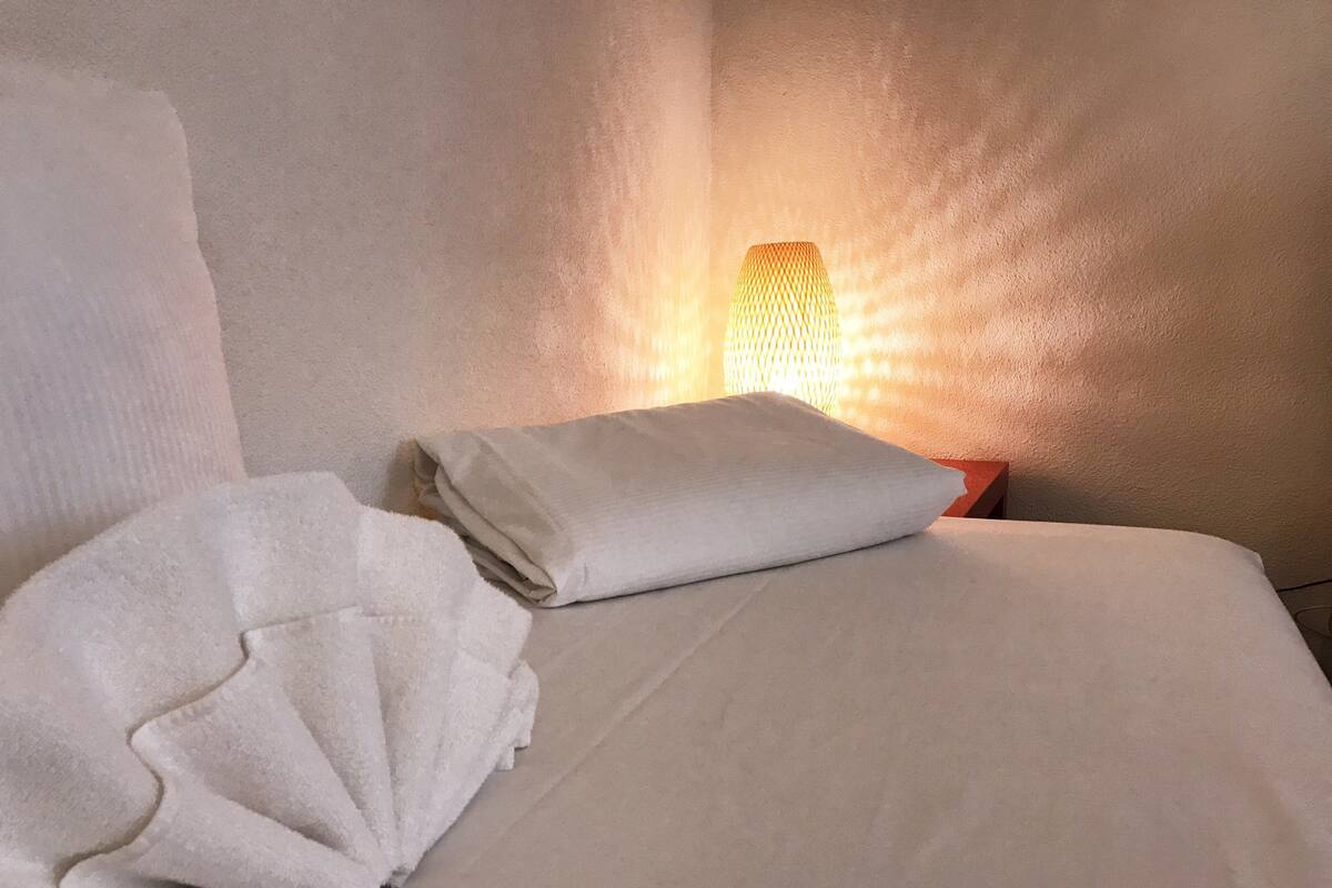 A neatly made bed with a white pillow and a folded white towel.