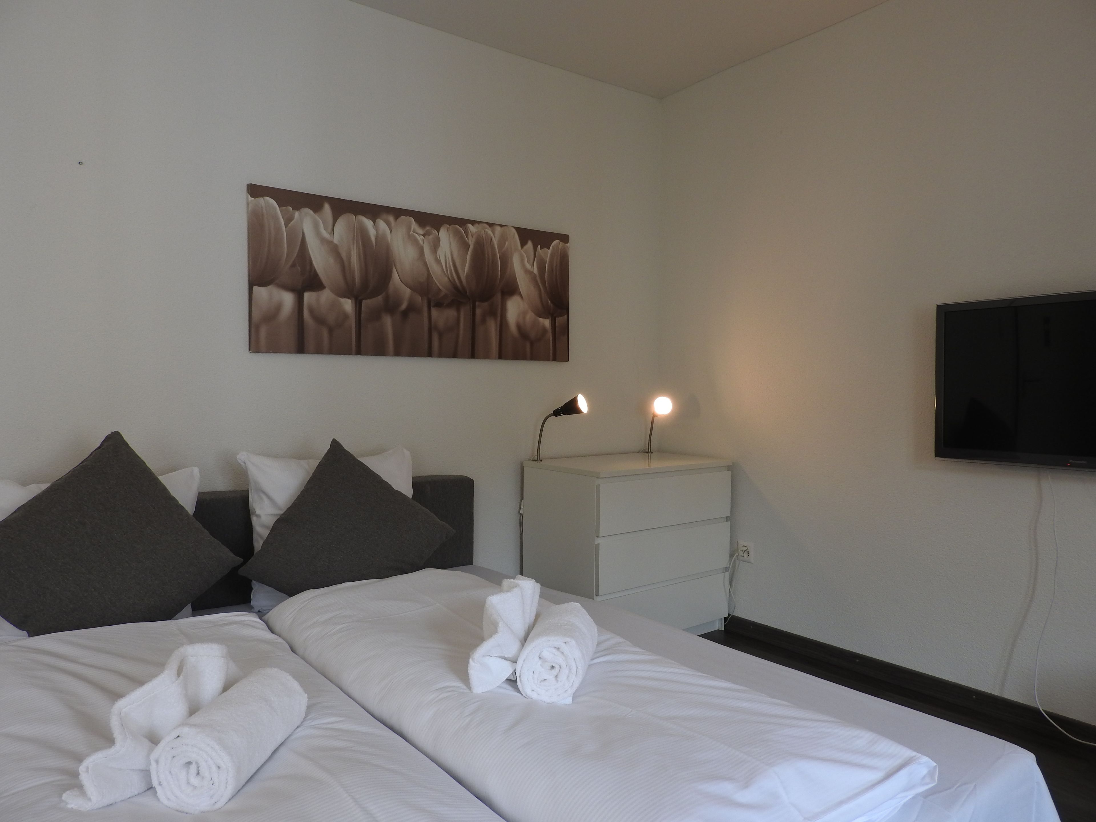 Une chambre d’hôtel comprenant un lit, des oreillers, une table de chevet avec une lampe, un téléviseur à écran plat et une œuvre d’art accrochée au mur.