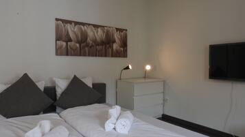 Une chambre d’hôtel comprenant un lit, des oreillers, une table de chevet avec une lampe, un téléviseur à écran plat et une œuvre d’art accrochée au mur.