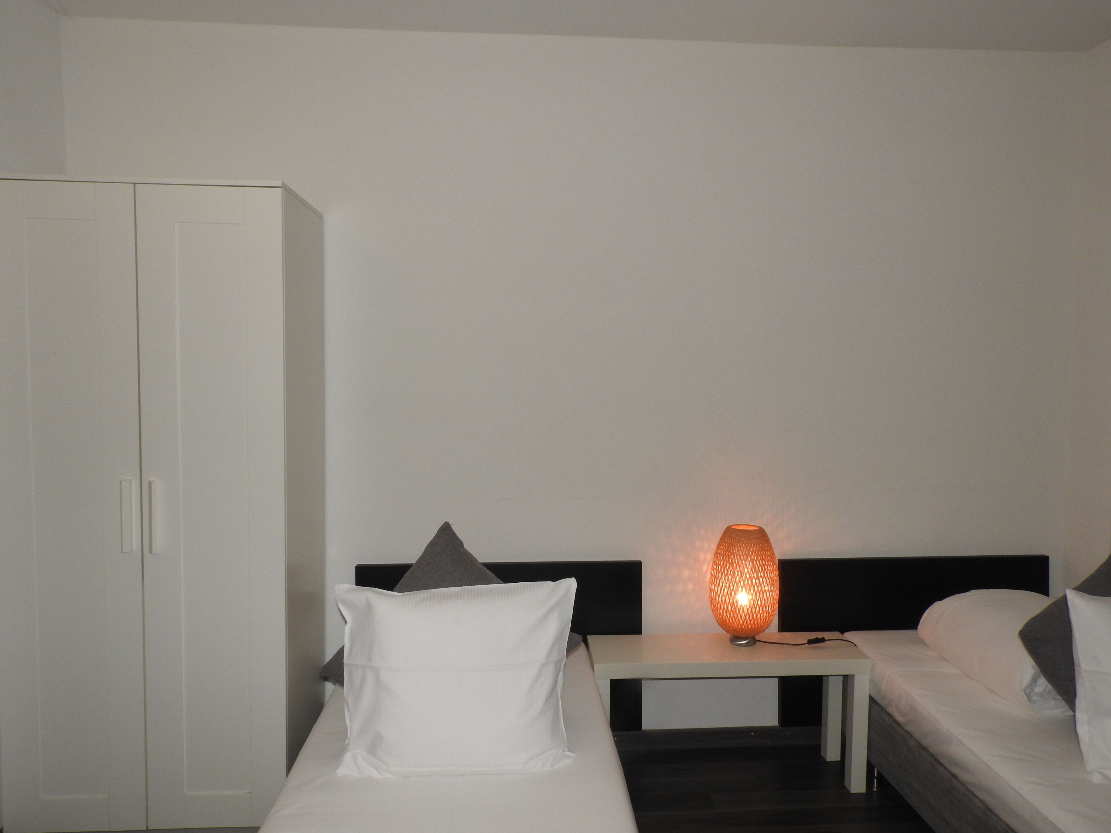 A hotel room with a bed, a bedside table, a lamp, and a wardrobe.