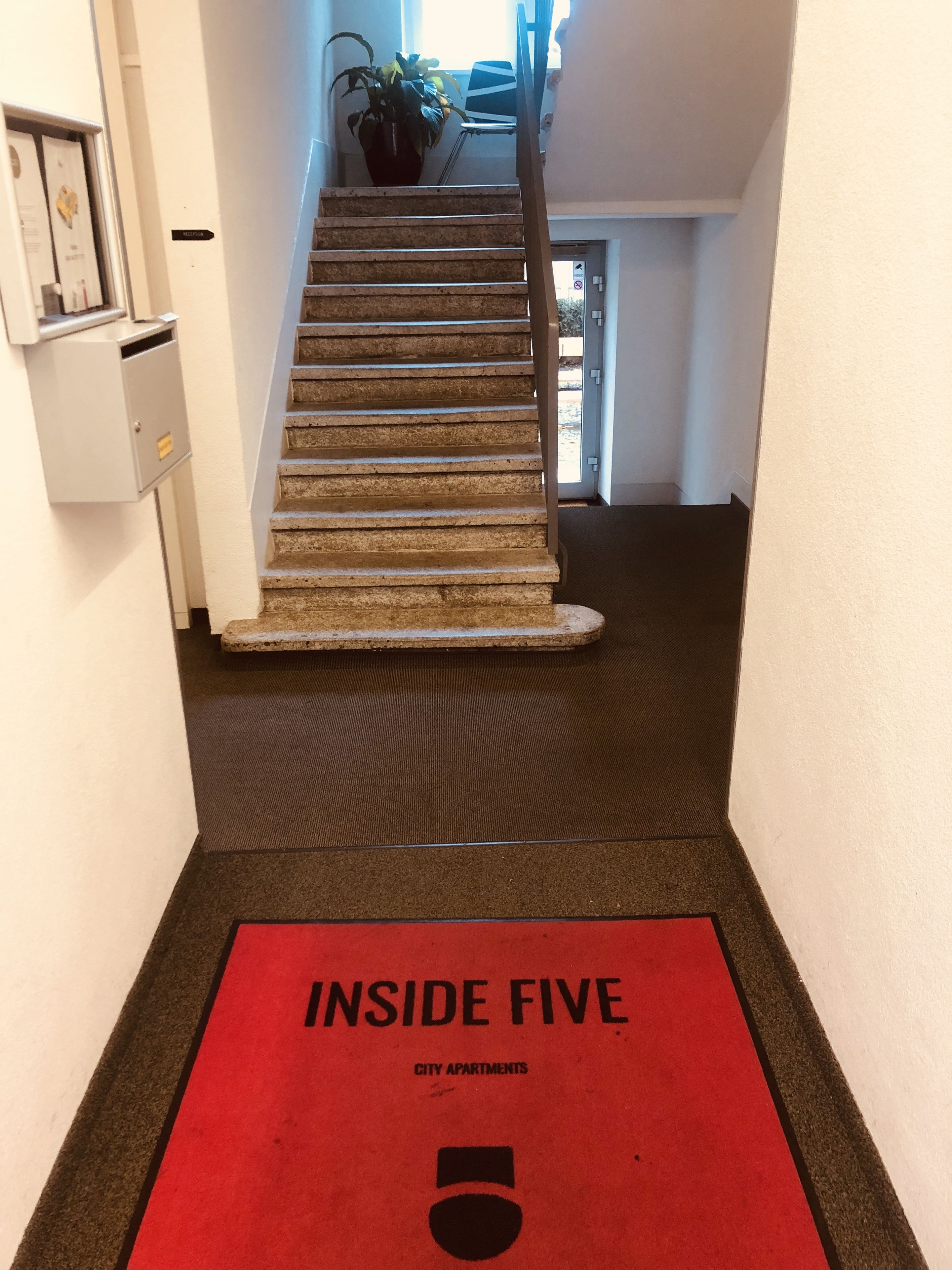 Una escalera con alfombra roja que conduce a una puerta con la leyenda 'Inside Five City Apartments'.