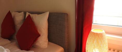 A bed with white and red pillows, a grey headboard, and a lamp on a bedside table.